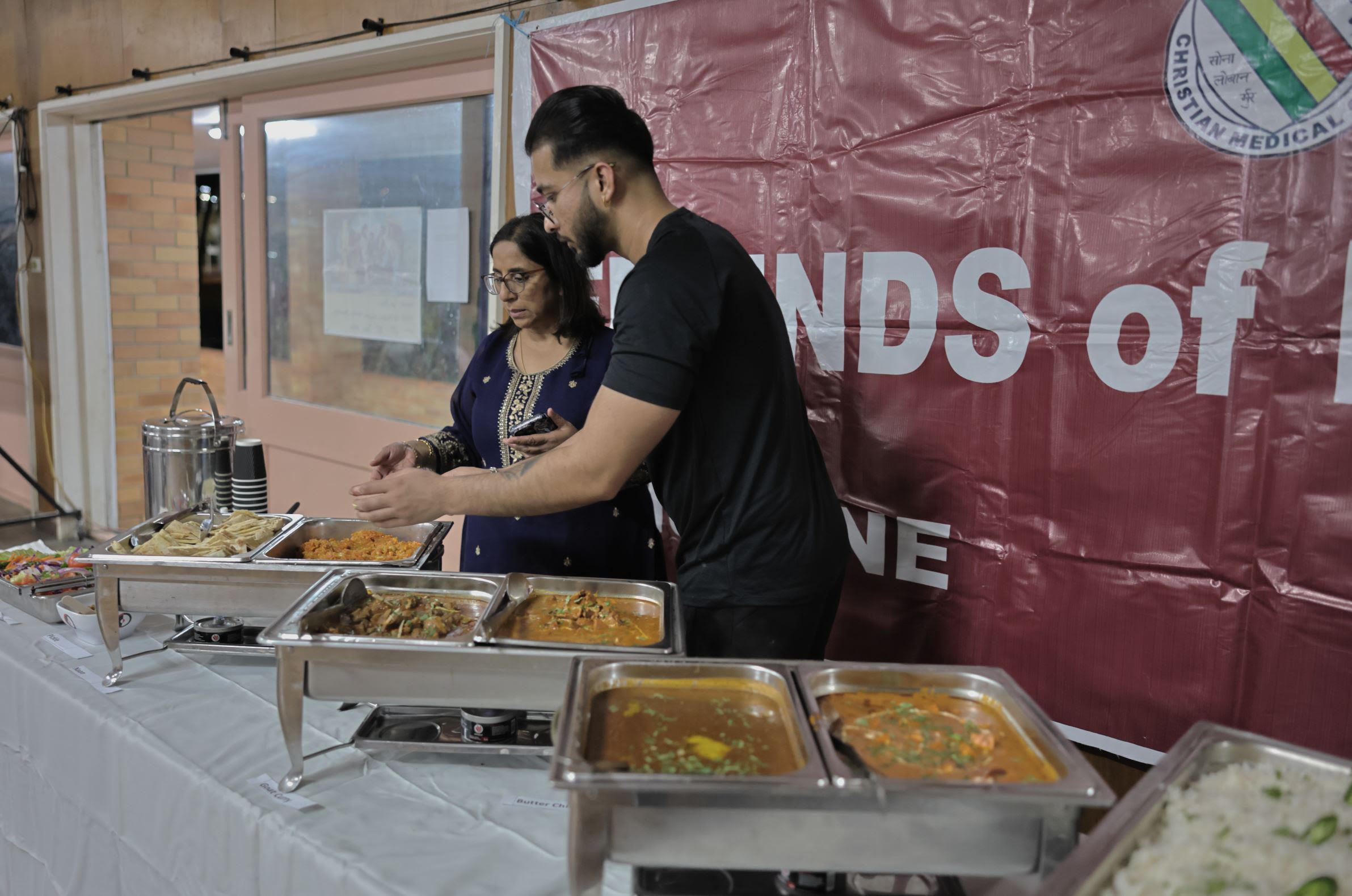 Volunteers serving food beside the Friends of Ludhiana banner